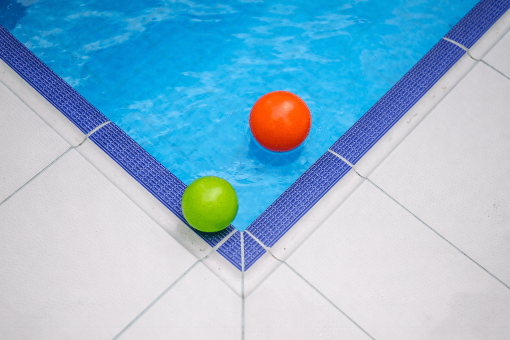 Two floating pool balls at the corner of a commercial swimming pool with blue water and tiled edge